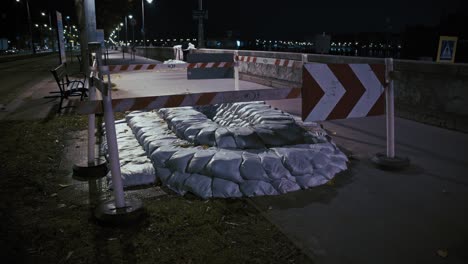 sandbags and barricades set up along a flooded riverside path at night in budapest