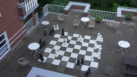 Oversized chess set on outdoor terrace with tables and chairs creates a playful scene