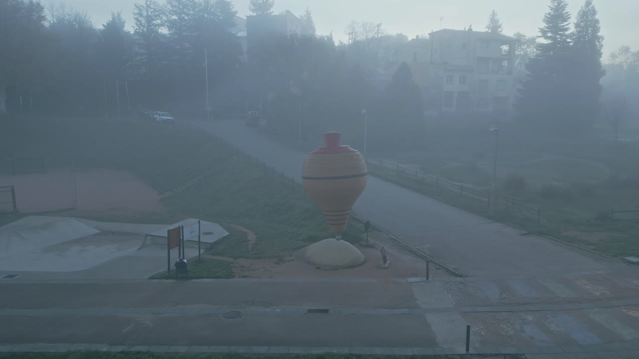 Misty morning landscape revealing foggy atmosphere enveloping sant hilari sacalm with monumental spinning top sculpture dominating serene urban scenery in catalonia, spain