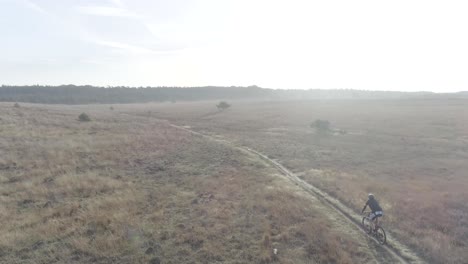 Tiro-De-Drone-De-Mountainbiker-Cabalgando-Hacia-La-Luz-Del-Sol