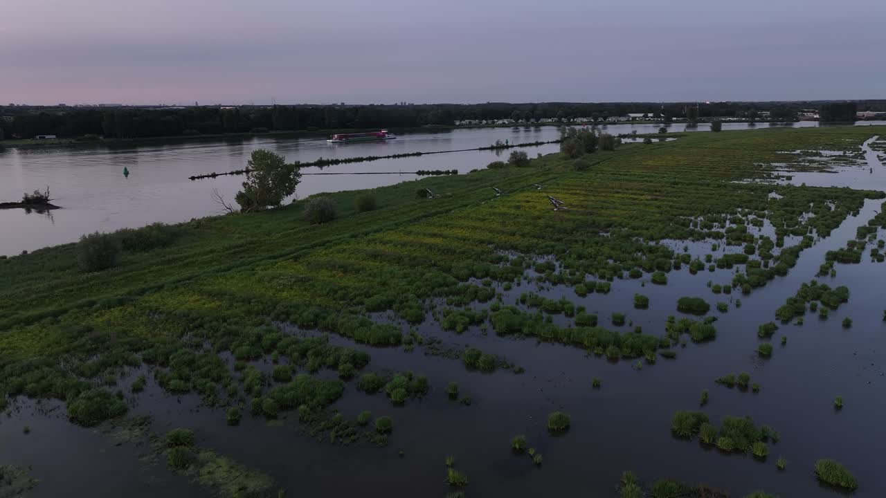 Flooded marshland at dusk with patches of green vegetation reflecting on calm water