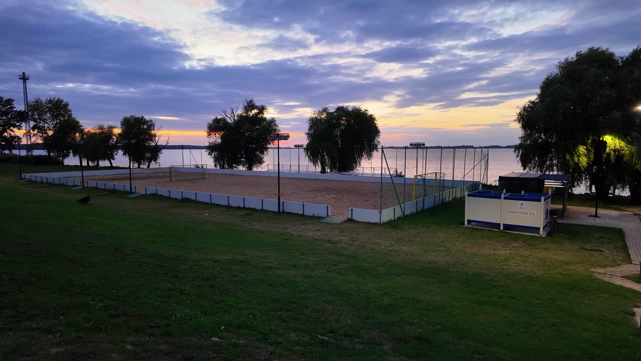 Two playful black, Long-Haired German Shepherd dogs run back and forth on the green grass of the Abadszalok beach after sunset at Lake Tisza, Hungary.