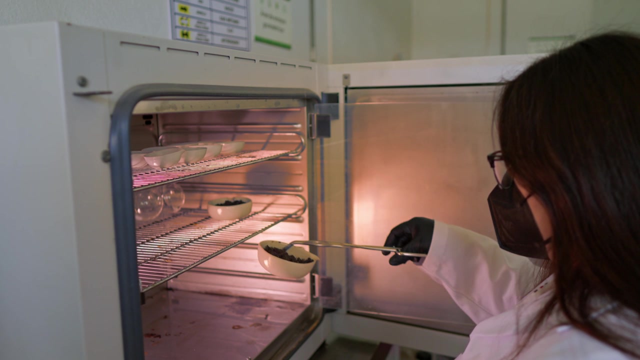 Scienziata con occhiali e mascherina rimuove campioni di terreno in porcellana da un'autoclave calda per l'analisi, parte di un progetto di agroindustria circolare in laboratorio