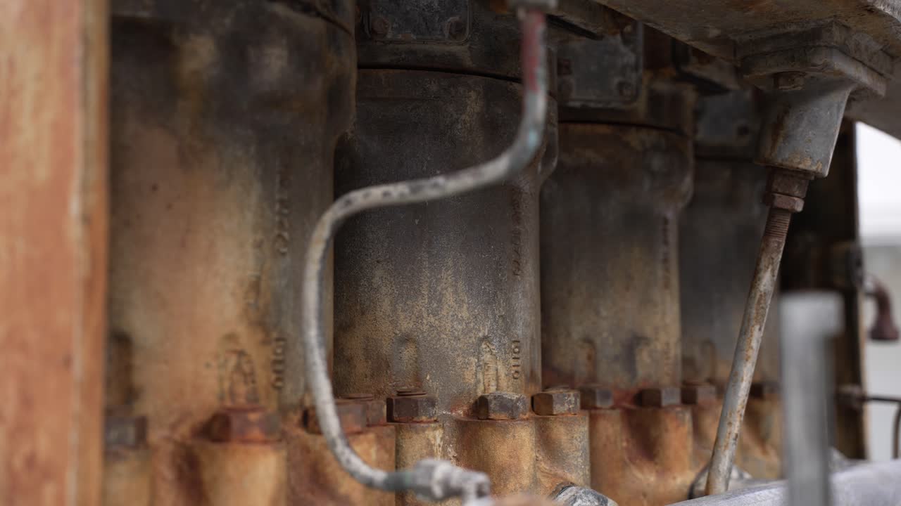 Rustne metalcylindre, bolte og rør fra en vintage industrimotor. Detalje af tungt maskineri.