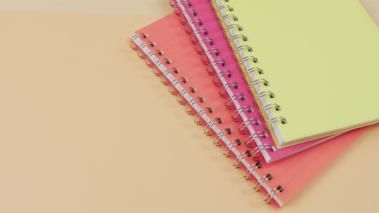 los cuadernos espirales coloridos están apilados en un fondo rosado y amarillo de doble tono, con espacio para copiar