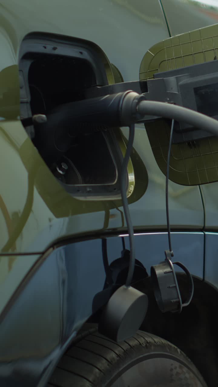 Vertical video Close up of electric cable attached to EV car charging port to recharge battery