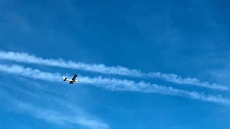 Vista-De-ángulo-Bajo-De-Un-Pequeño-Avión-De-Hélice-En-El-Cielo-Azul-Con-Estelas-Químicas