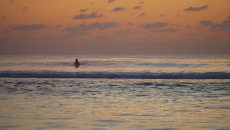 Unrecognizable-backlit-tourist-inside-the-sea-waves-during-orange-dusk-sunset