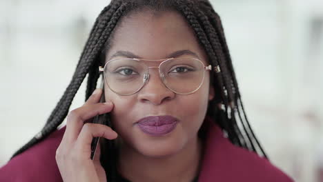 Closeup-of-Afro-American-young-girl-with-plump-rose-lips-and-braids-in-aviator-eyeglasses-wearing-rose-coat