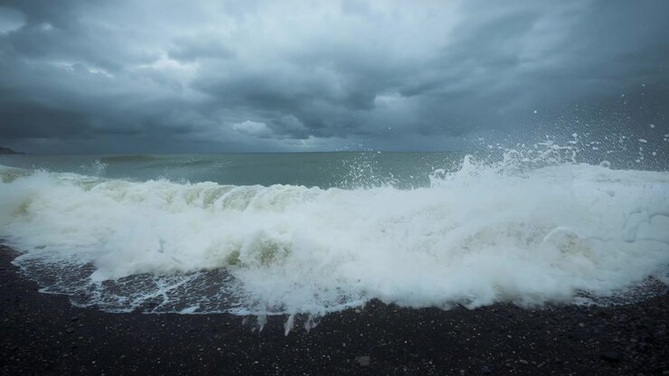 Vague océanique s'élevant et s'enroulant, déferlant, poussée par les vents de tempête, s'abattant sur un rivage de galets avec de l'écume.