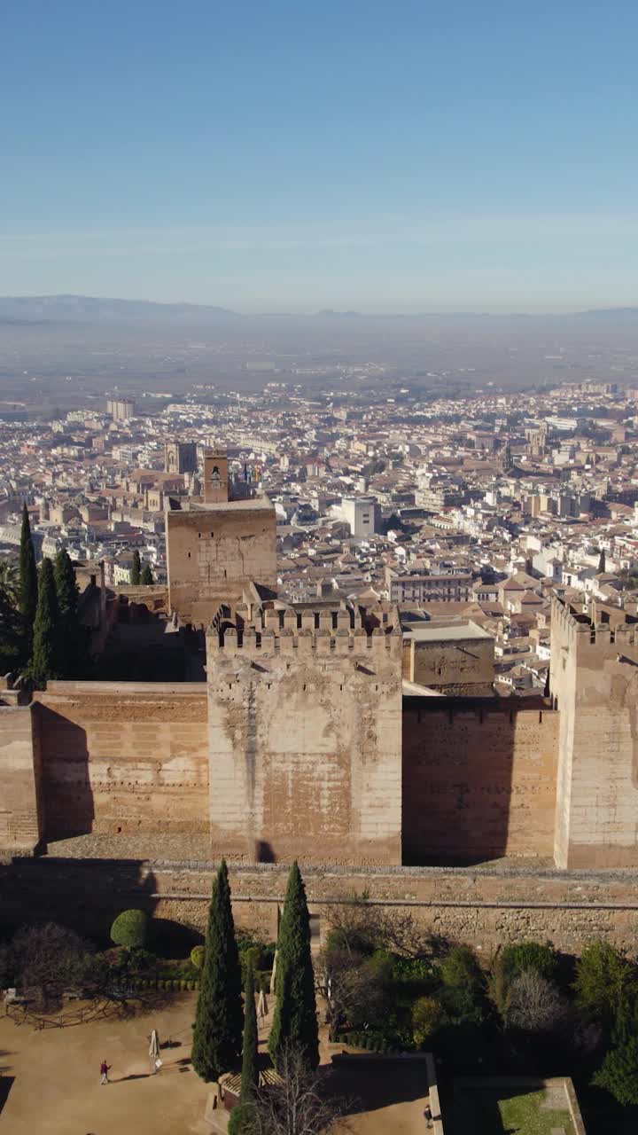 Sobrevoo da Alhambra em Granada, mostrando o Palácio de Carlos V e a Alcazaba com a paisagem urbana ao fundo. Aéreo vertical.