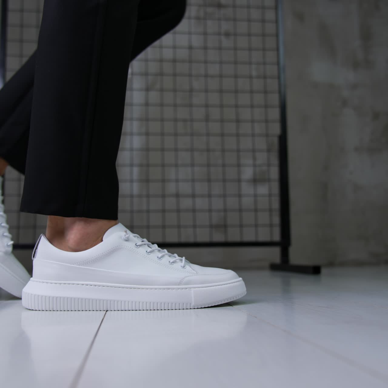 Stylish snow-white sport shoes with laces on a model. Man wearing black trousers and modern sneakers posing in studio. Close up