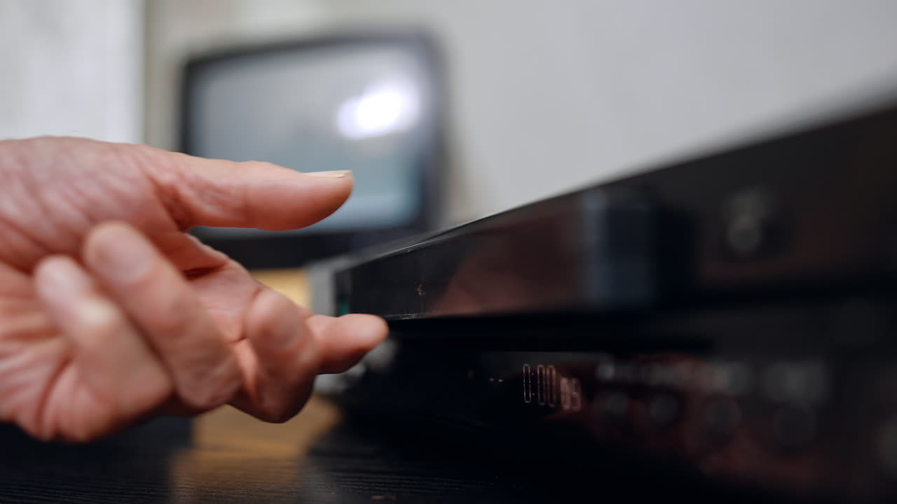 DVD tape shoots out of the player. Close up. Senior male's hand takes the tape out of device