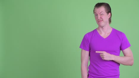 studio shot of young man looking disgusted and pointing finger to copy space against green background