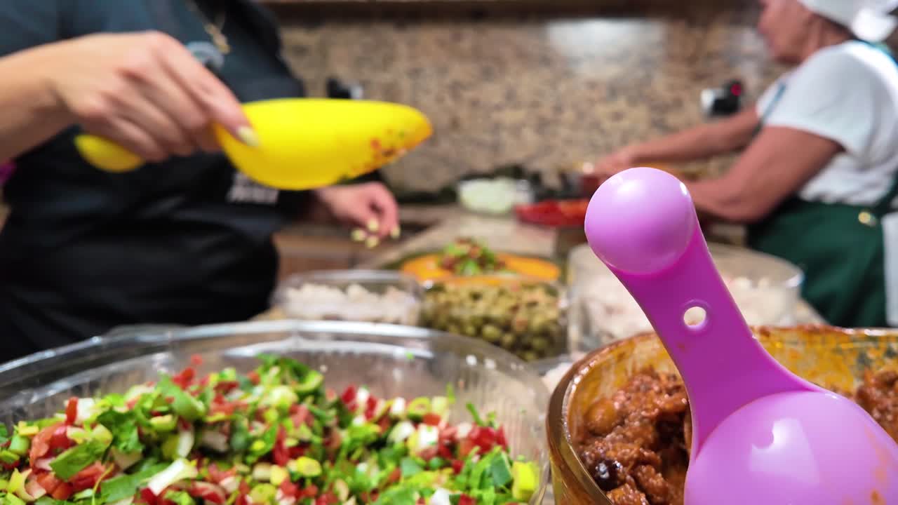 Due donne latine che preparano hallacas tradizionali venezuelane in una cucina rustica, aggiungendo i ripieni e lavorando insieme, una scena di cucina casalinga festiva.