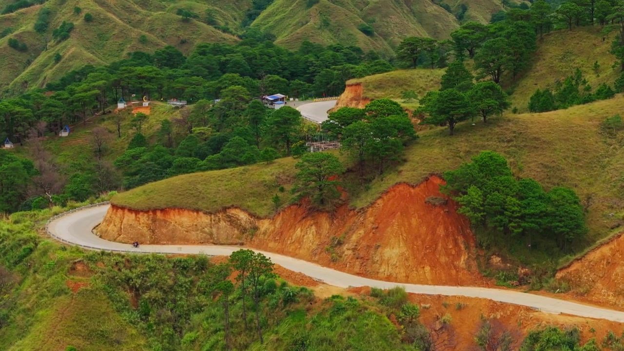 Pengendara sepeda motor melintasi jalan raya lereng bukit terpencil di samping tebing terjal dan hutan pinus