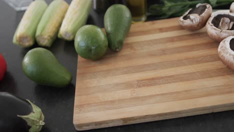 close up of kitchen countertop with wooden chopping board and vegetables, slow motion