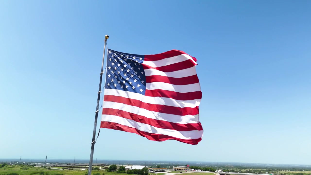 Filmisk stockoptagelse af det amerikanske flag, der vajer stolt i den stærke vind under skarpt sollys. B-roll af høj kvalitet til patriotiske og kommercielle projekter.