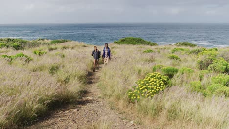 Pareja-Diversa-Usando-Mochilas-Usando-Bastones-De-Marcha-Nórdica-Haciendo-Caminatas-En-El-Campo