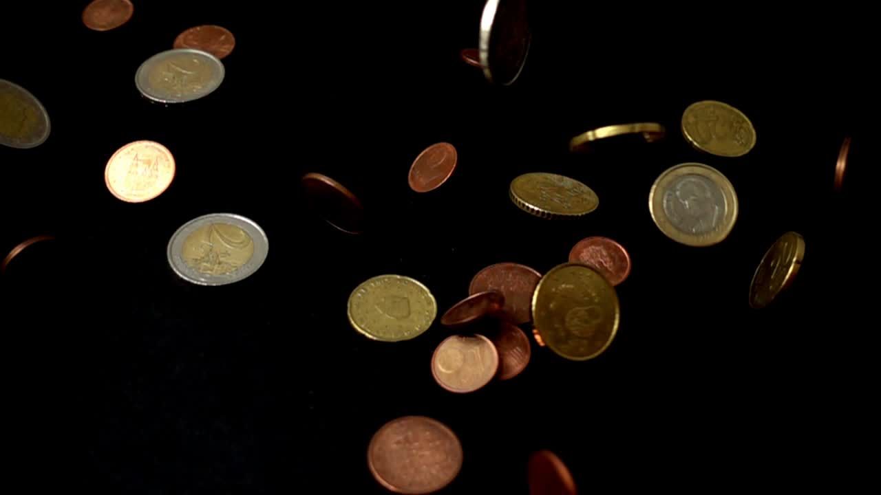 Coins fall on a black background. Slow motion