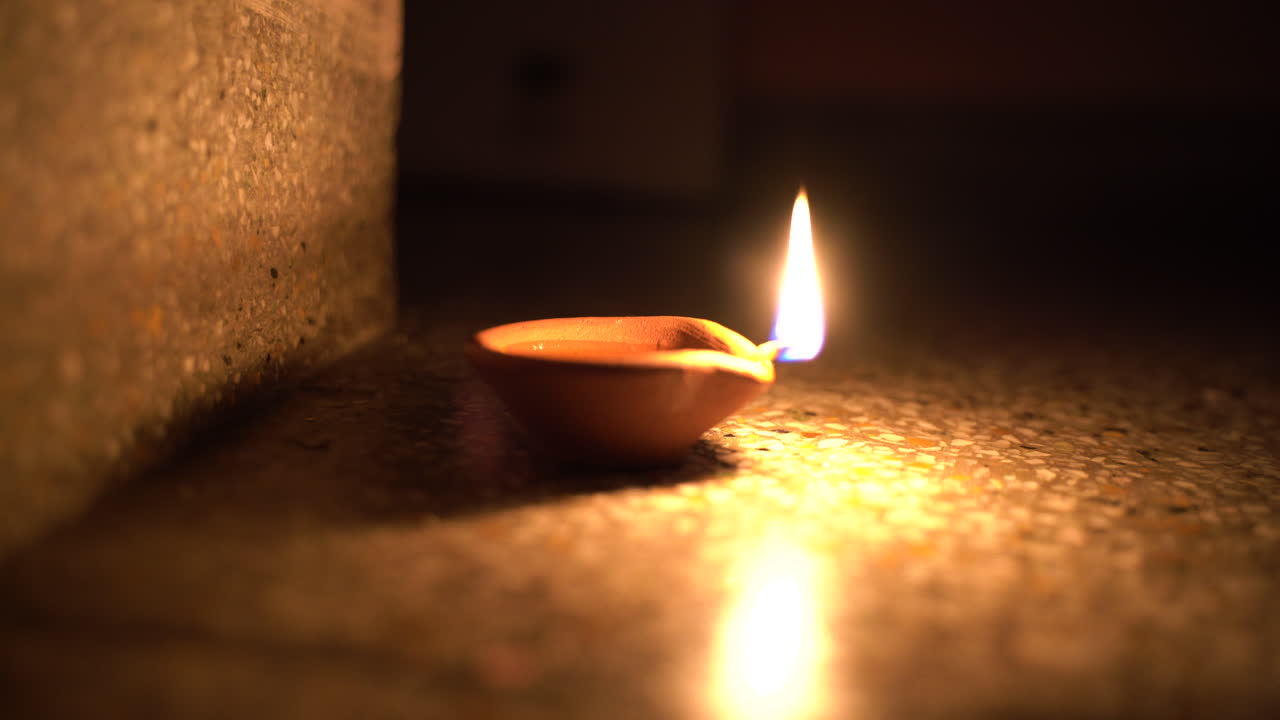Mani che accendono una diya (candela) di argilla a olio in una stanza buia durante il festival di Diwali, il sacro festival delle luci dell'India
