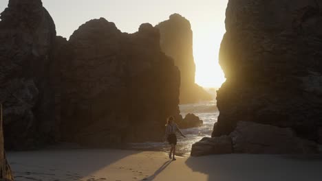 woman walking on a beach at sunset with rocky coastline