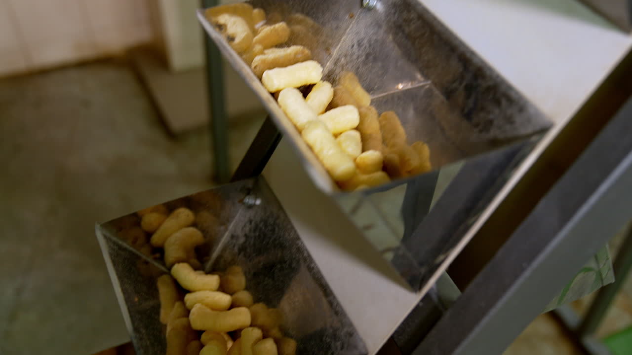 Rising conveyor belt with metal pockets full of snacks. Corn sticks manufacturing at food factory close up.