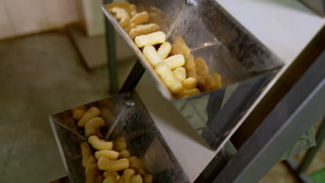 rising conveyor belt with metal pockets full of snacks. corn sticks manufacturing at food factory close up.