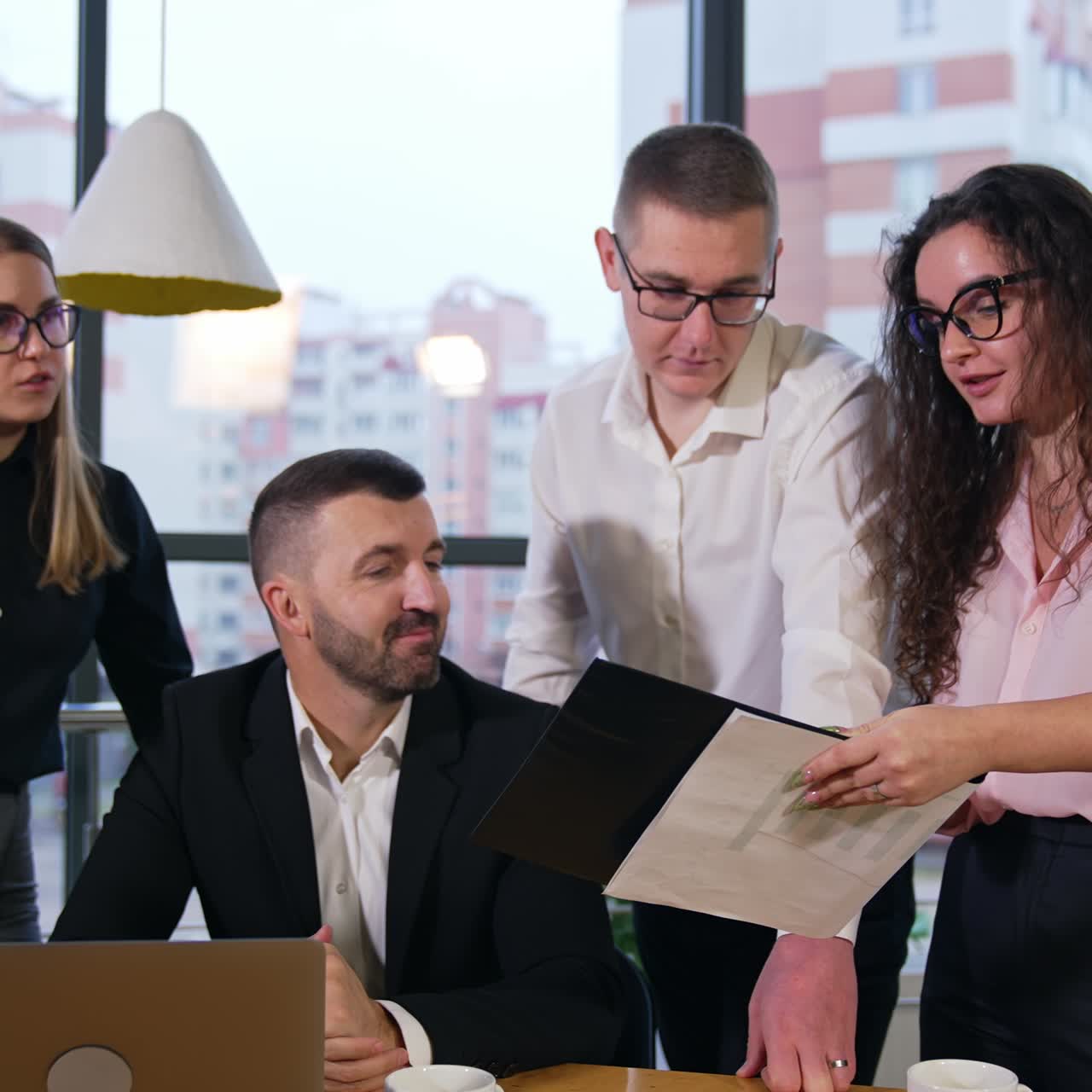 Long-haired brunet woman holding documents in her hands showing them to colleagues. Office team approve what they hear and nod heads