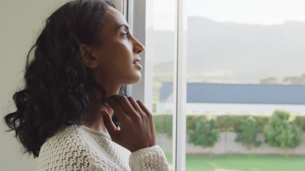 mujer biracial feliz mirando por la ventana y sonriendo