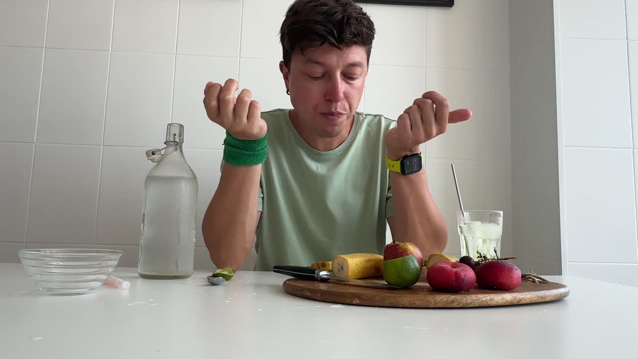 Giovane uomo che mangia frutta fresca al tavolo della cucina.