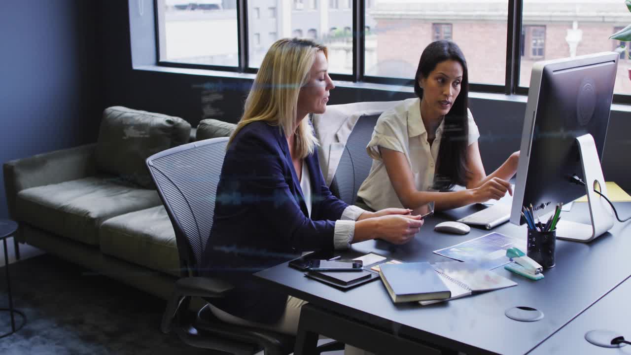 Two staff leaning toward monitor, pointing and checking business data as waveforms sweeping screen