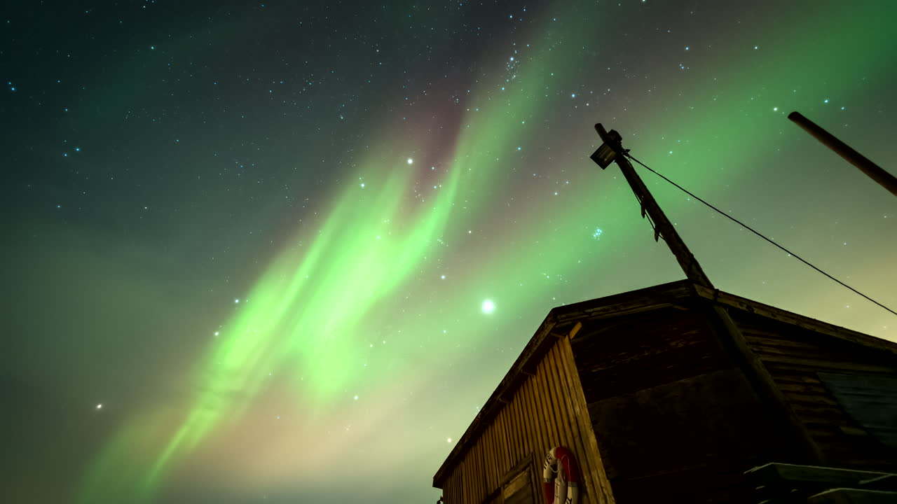 Mesmerizing northern lights flaring in sky over wooden boat house, time-lapse
