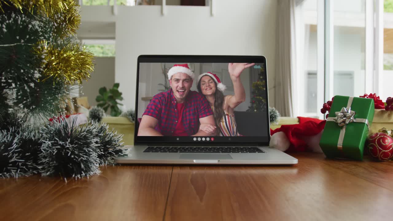 una pareja caucásica sonriente con sombreros de santa claus en una videollamada de navidad en una computadora portátil