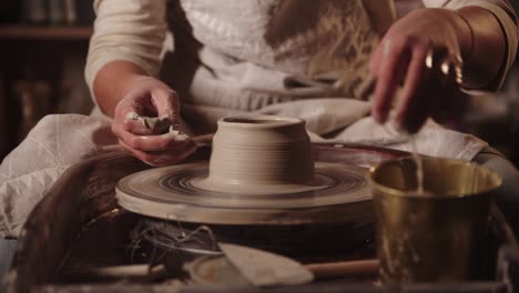 young woman potter wetting her hands and forming the clay with her fingers