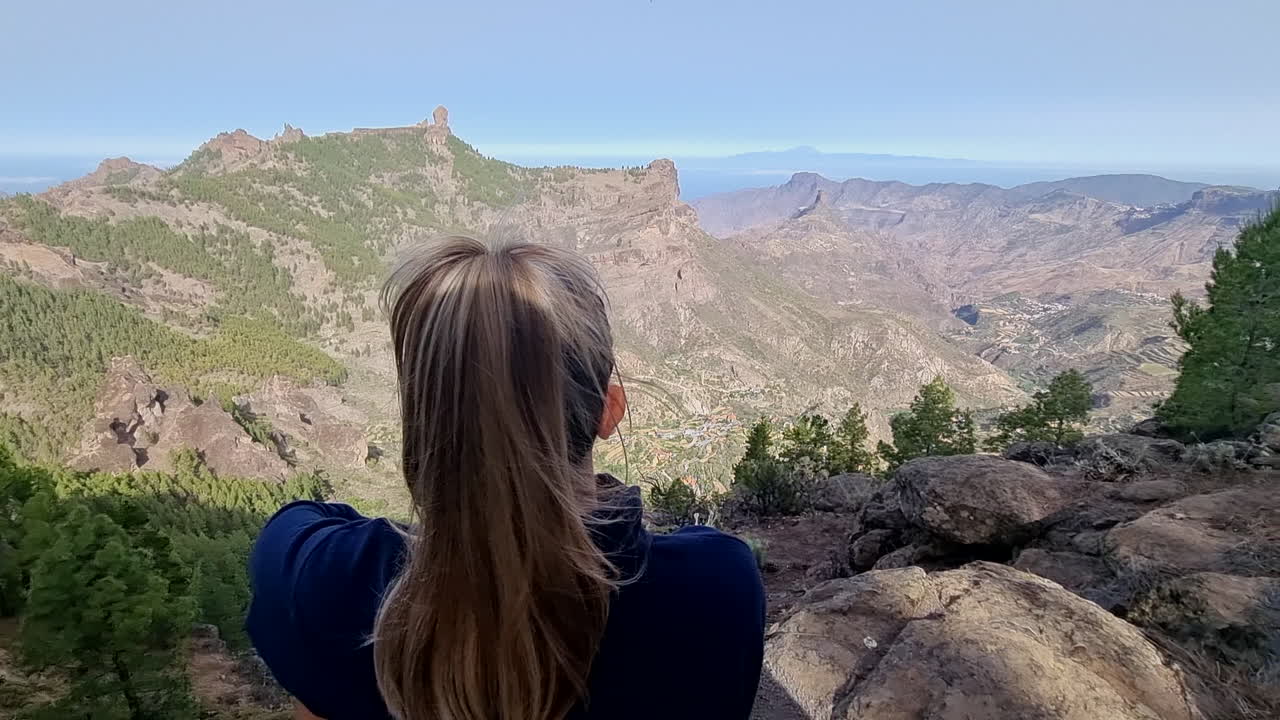 chica rubia irreconocible observa la vista y el roque nublo desde la cima de una montaña de espaldas al espectador