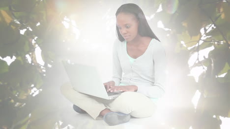 animation of african american woman sitting using laptop over leaves