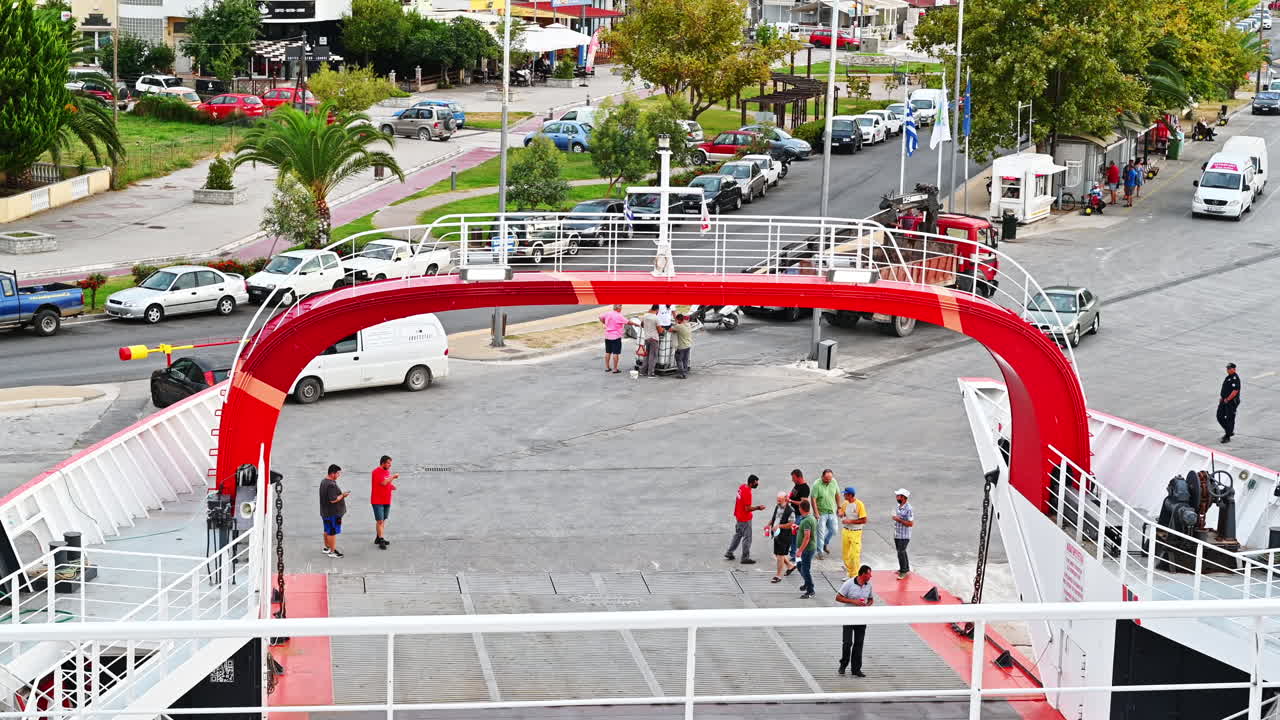 THASOS, GREECE - SEPTEMBER 23, 2020: Moored ferryboat, opened gangplank in the port, road, walking people, town and parked cars on the background