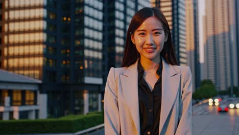 professional asian businesswoman confidently standing in modern urban environment, golden sunset illuminating cityscape behind her, symbolizing career success and leadership potential