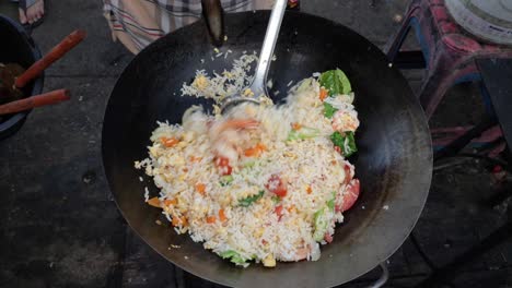 stirring and cooking fried rice with vegetables in wok at open air kitchen - overhead medium shot