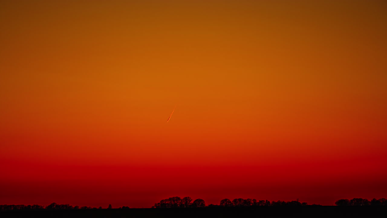 línea brillante de rastro de avión en el cielo rojo bajo un horizonte oscuro