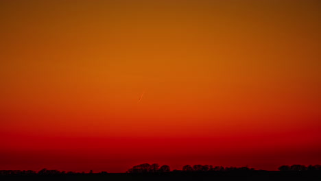 línea brillante de rastro de avión en el cielo rojo bajo un horizonte oscuro