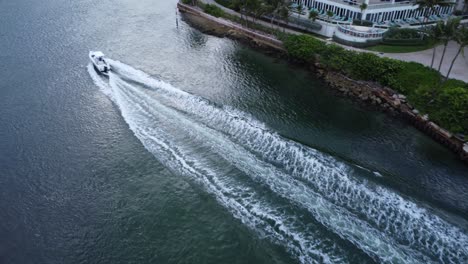 speed boat heads out to sea along a river between housing and apartments from an aerial drone shot following the boat