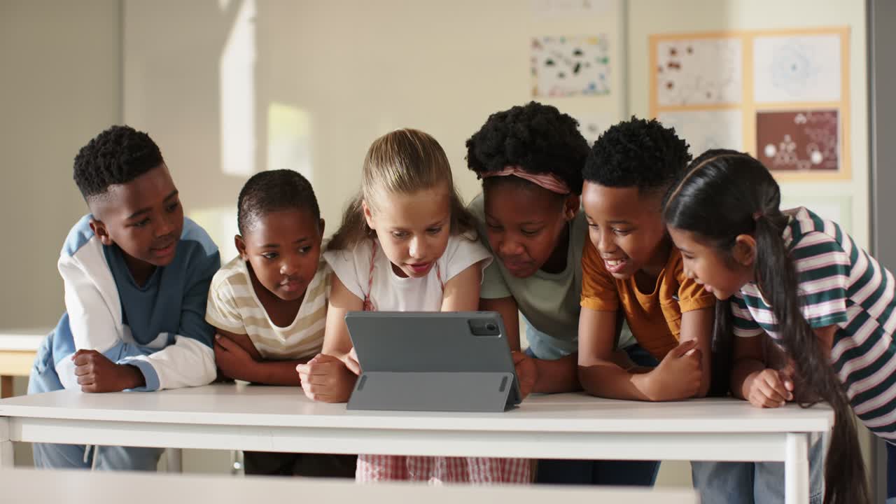 Compagni di classe adolescenti chinati su un tablet su un tavolo bianco a scuola, che reagiscono al contenuto dello schermo