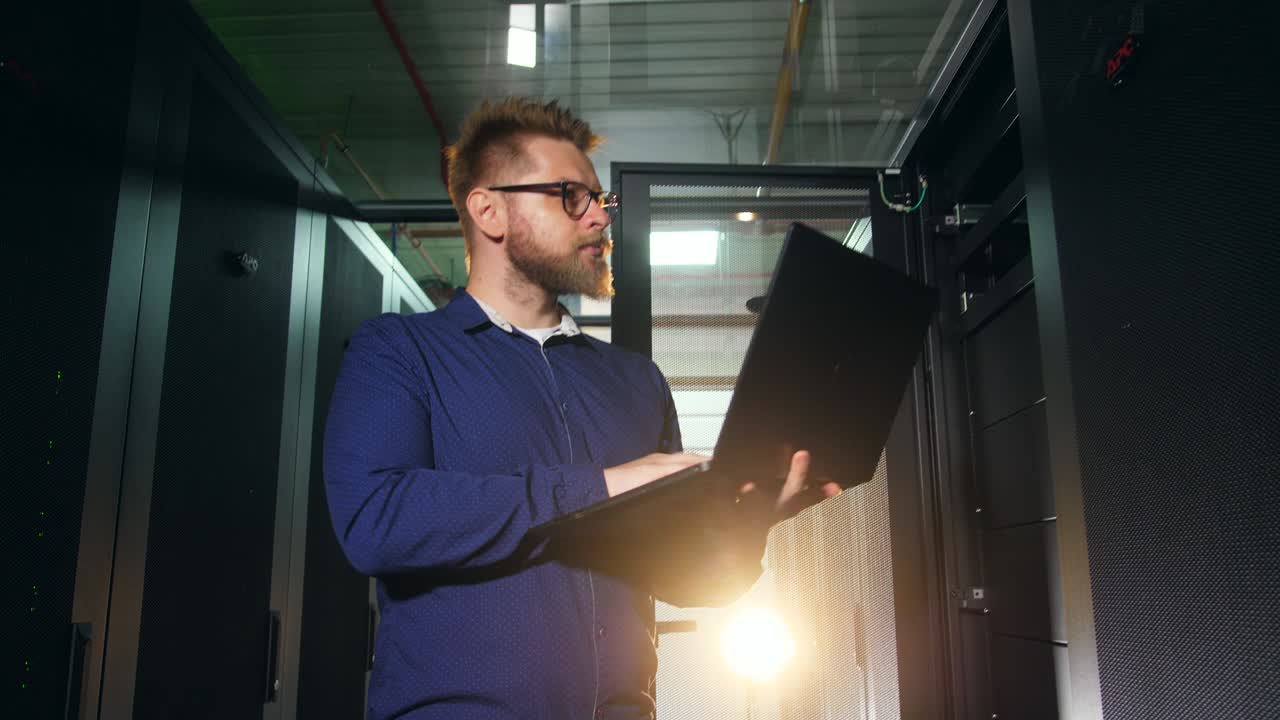 ingeniero informático escribe en portátil mientras trabaja en la sala de servidores.