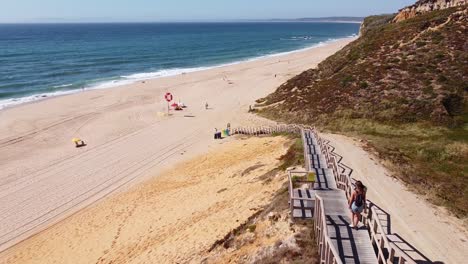 Playa-Praia-Das-Bicas-En-Castelo,-Alentejo,-Costa-Oeste-De-Portugal---Vista-Aérea-De-Drones-De-Una-Chica-Turista-Caminando-Por-La-Escalera-A-La-Playa-De-Arena-Dorada