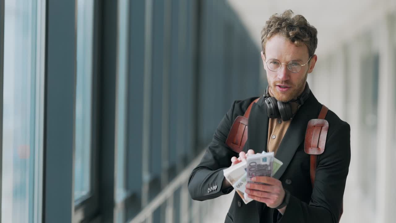 Stylishly dressed man shows bundles of money to the camera