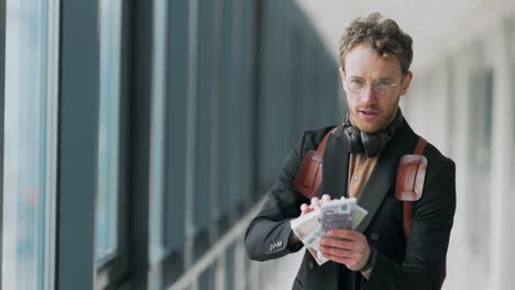 stylishly dressed man shows bundles of money to the camera