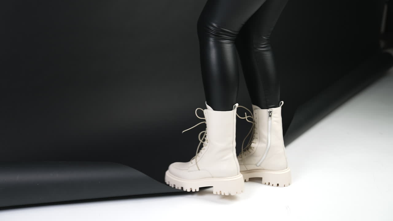 White combat boots on tractor soles. Model in black pants standing with her back to camera on a black and white backdrop.