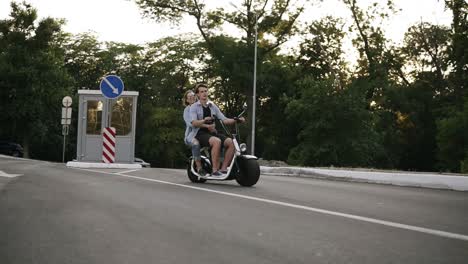 Vista-Lateral-De-Una-Pareja-Andando-En-Bicicleta-Y-Divirtiéndose.-Hermosa-Joven-Y-Hombre-Conduciendo-Por-La-Ciudad.-Libertad,-Estilo-De-Vida-Feliz